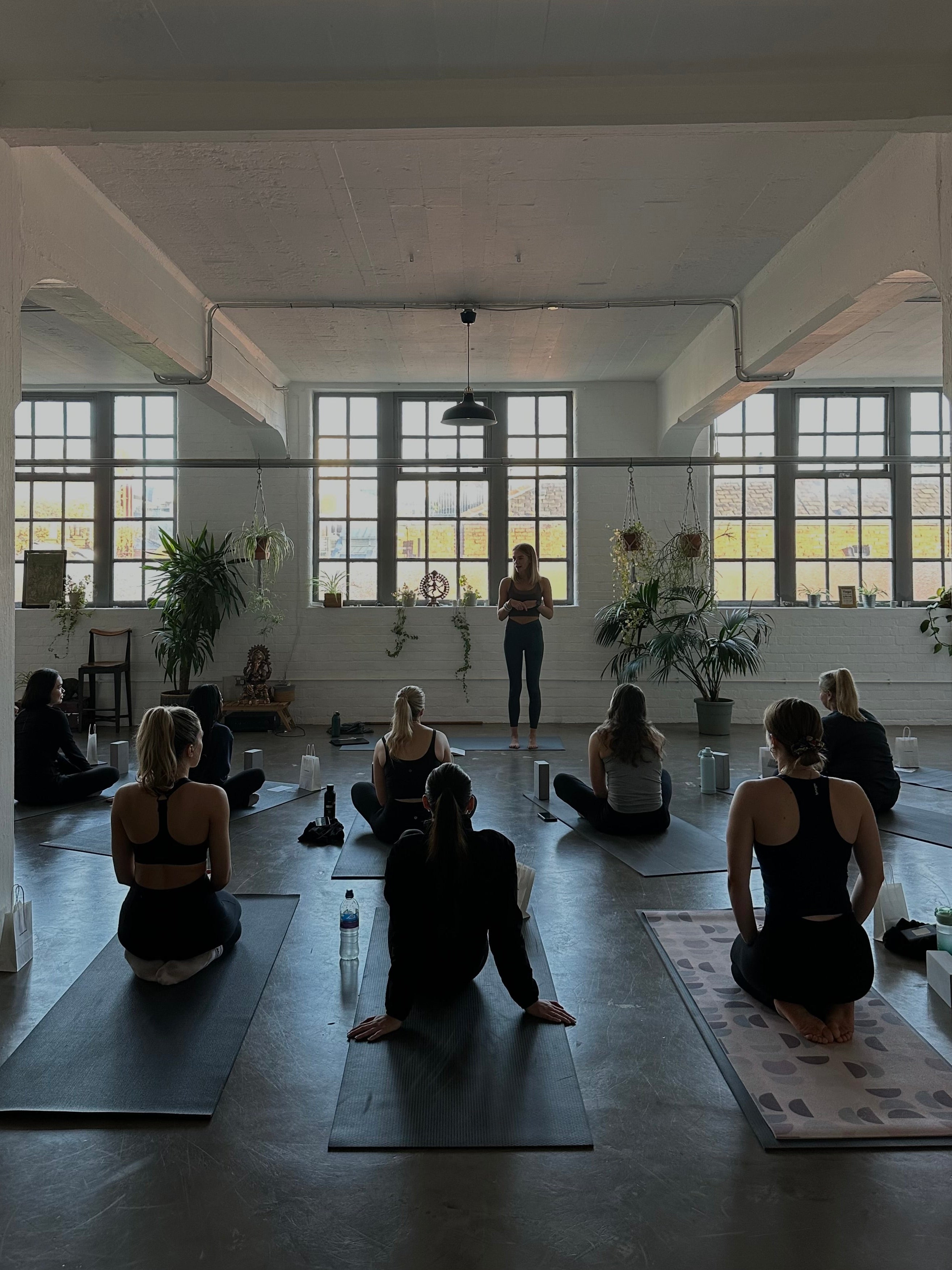 Group of people practicing yoga in a large, well-lit room with large windows.